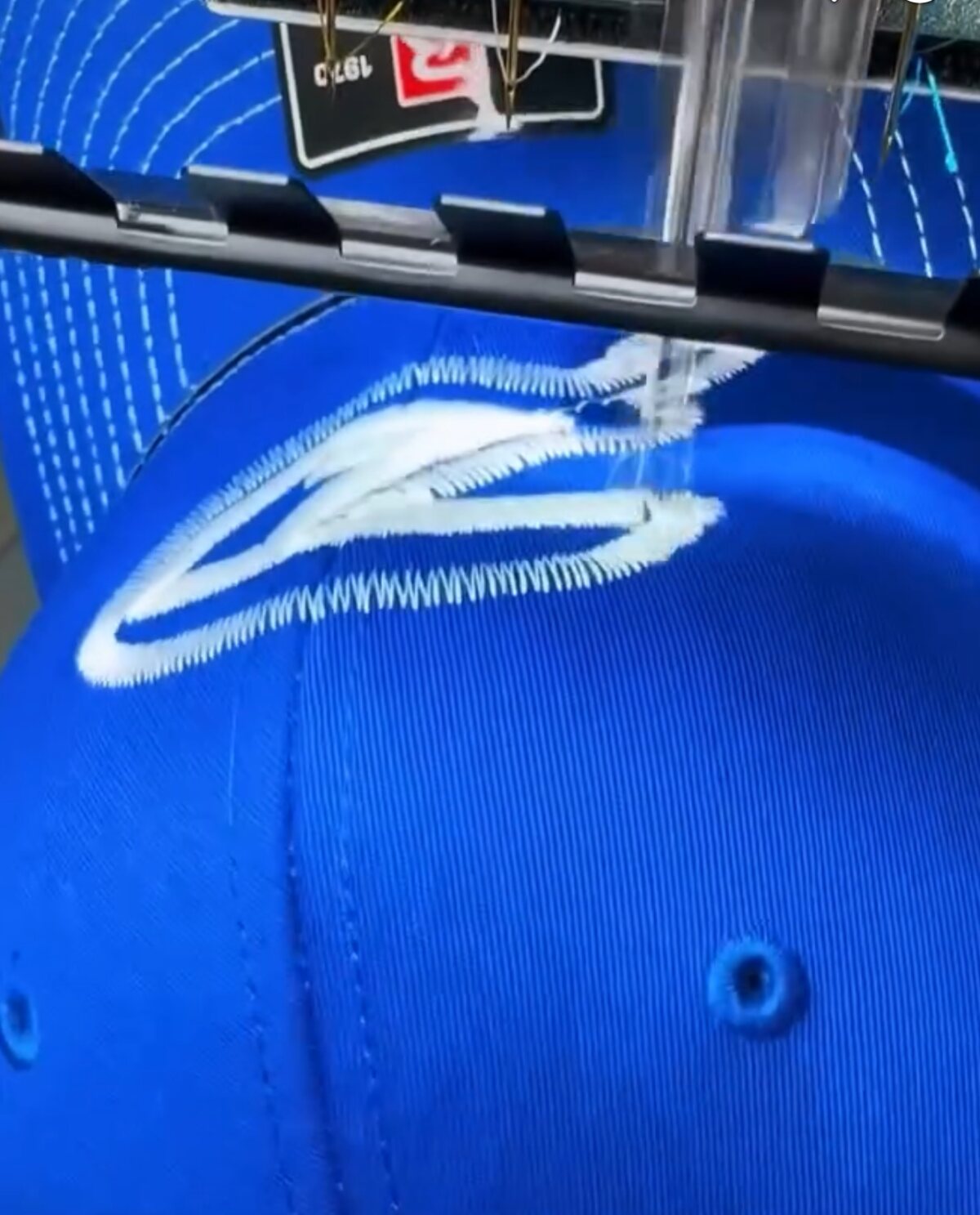 An embroidery machine stitching a white monogram into a royal blue trucker cap
